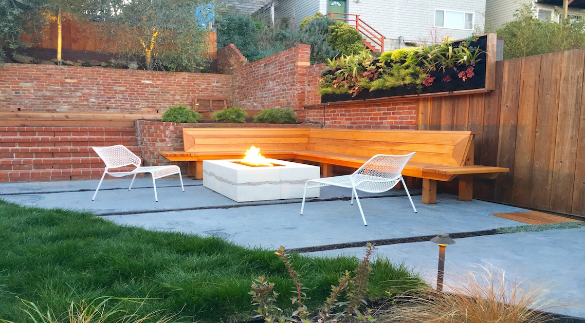 back yard featuring stone firepit with built-in bench and seating area with brick walls and terraces in the background.