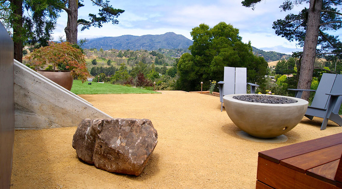manicured stone and gravel yard featuring a round concrete firepit and seating area with a wide view of landscape and hills in the background.