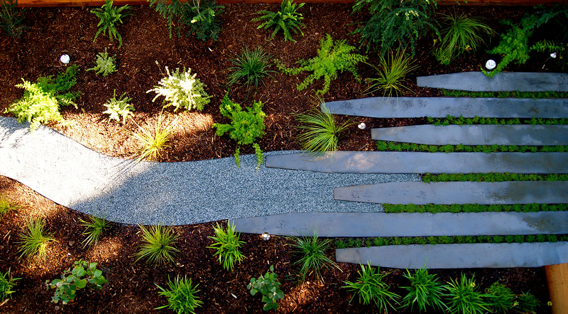 overhead view of backyard with outdoor lamps, paved walkway and plant beds