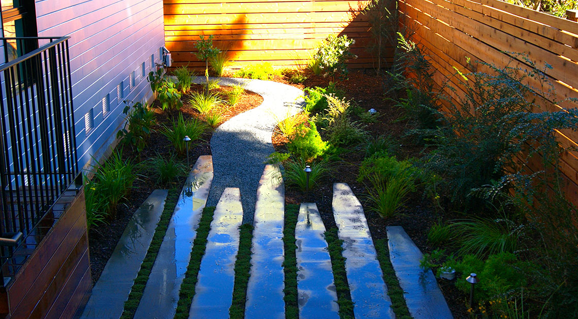 reverse view of backyard with outdoor lamps, paved walkway and plant beds