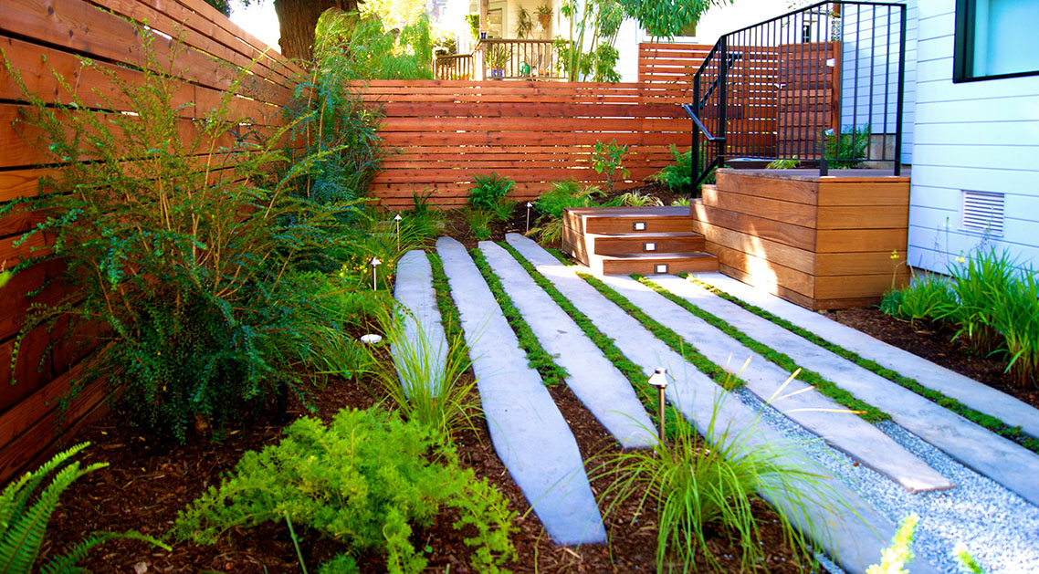 daytime view of backyard with outdoor lamps, paved walkway and plant beds
