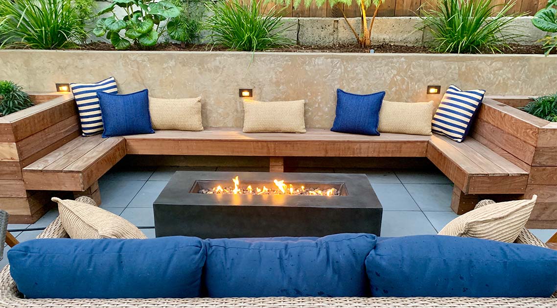 paved back yard with built-in wooden benches and cushions around a raised fire pit